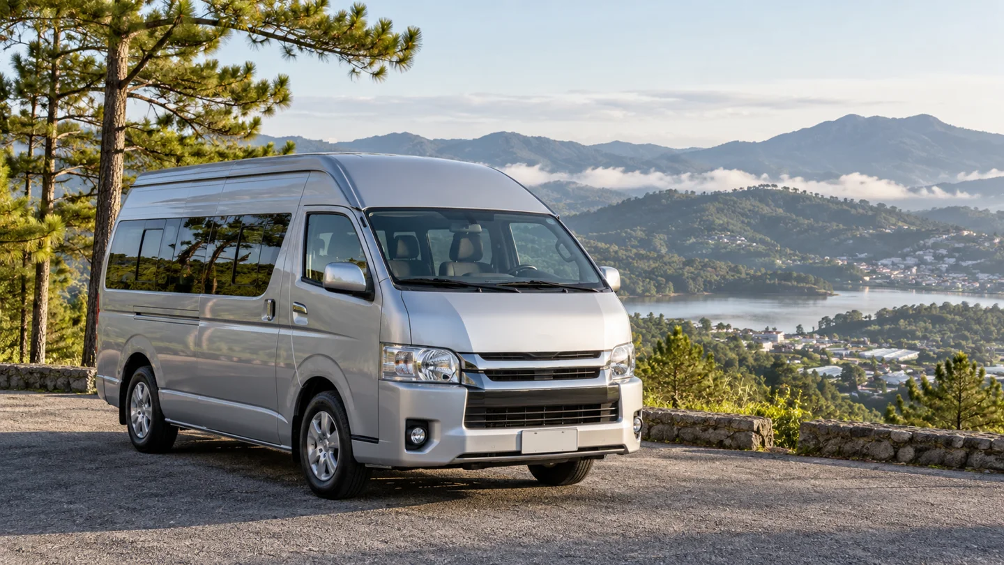 Minibus bạc chụp góc phía trước trong bối cảnh đồi và cây thông